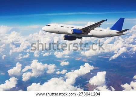 Commercial airliner flying above clouds with blue sky in background.
