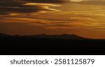 Commercial airliner on its approach slope while preparing to land along a silhouetted mountain range under hazy desert sky. 
