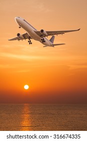 Commercial Airplane Flying Over The Sea At Sunset