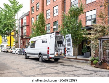 Commercial compact cargo small size white mini van delivered goods to client at multi-apartment high-rise building and standing on the autumn street of urban city waiting for unloading