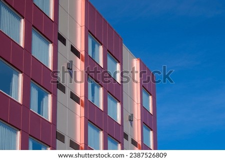 Commercial external metal composite panels on a building with blue sky and clouds in the background. The durable metal composite panels are both red and grey in color on the modern building.