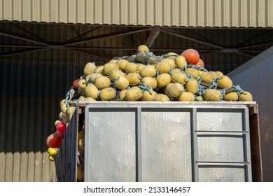 A commercial fishing net piled in a metal storage container. The industrial net is a green braided rope with plastic cork floats or small yellow and orange color buoys. The nets have edge markers.