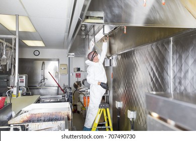 Commercial kitchen worker washing up at sink in professional kitchen