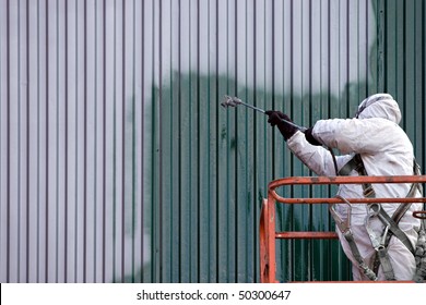 A Commercial Painter On An Industrial Lift Spray Painting A Steel Exterior Wall Or Duct.