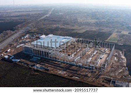 Commercial real estate of a large logistics business. Construction of a logistics center outside the city: concrete frame - piles and rafters with roof. Construction site - aerial drone view.
