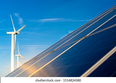 Commercial Solar Panel With Large Wind Turbines Behind On A Clear Day