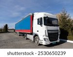 Commercial vehicle for business transportation. Semi-trailer tractor with a white cab and a long blue trailer. ten wheeler truck parked on a sunny day against the sky, front and side view.