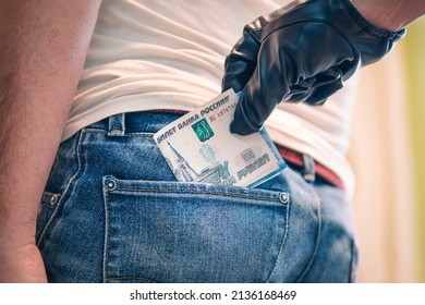 Committing a crime, stealing money from the back of jeans pocket, close-up. a black-gloved hand pulls the money out of his back pocket. The concept of petty crime and theft.