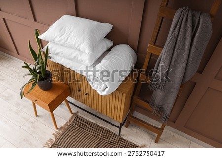 Commode with coffee table, blanket and pillows near brown wall in living room