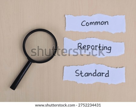 Common reporting standard (CRS) text handwritten on torn paper strips with magnifying glass over wooden background. Represents international tax transparency, financial regulations, and global information exchange