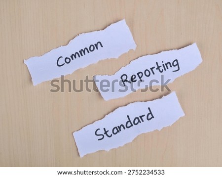 Common reporting standard (CRS) text handwritten on torn paper strips over wooden background. Represents international tax transparency, financial regulations, and global information exchange