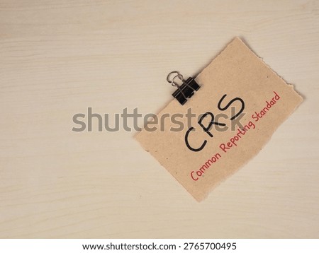 Common Reporting Standard (CRS) text on brown torn paper note with binder clip on wooden desk. Concept for global tax information exchange, financial transparency, and international banking regulations