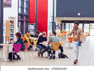 Communal Area Of Busy College Campus With Students Working At Tables And Tutor On Phone