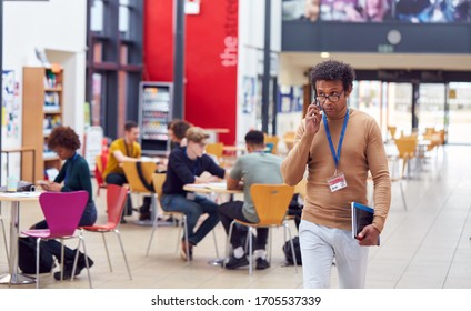 Communal Area Of Busy College Campus With Students Working At Tables And Tutor On Phone