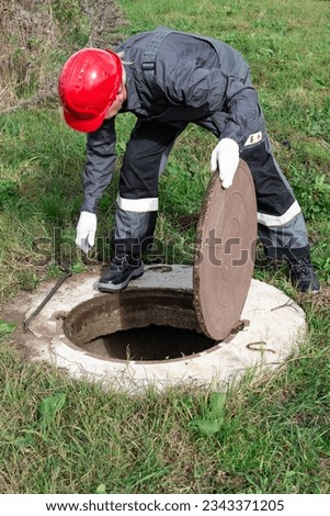 The communal worker opened the sewer hatch and looks inside. Inspection and maintenance of water wells and sewer wells.