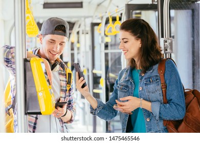 Communication, acquaintance, friendship concept. Young female asking for help handsome male with backpack for paying ticket with smartphone and ticket machine in modern tram during ride. - Shutterstock ID 1475465546