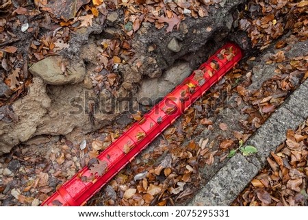 Communication Cables covered by red plastic flexible tube, Network Buildout high-speed Internet Network cables in red Cable Protector Wire Cover are buried underground on Construction site. 