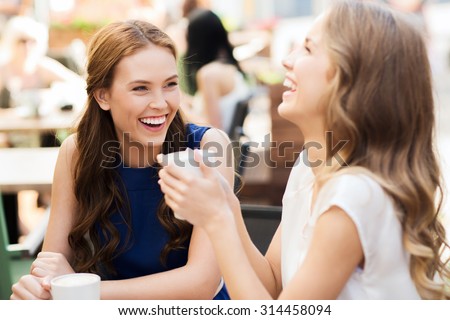 communication and friendship concept - smiling young women with coffee cups at cafe