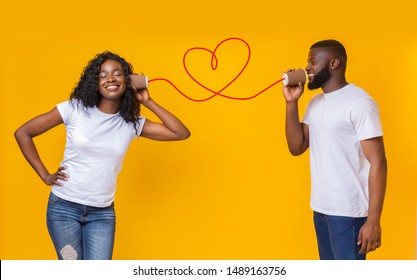 Communication And Fun. Young Black Couple Talking Through Tin Can Phone, Yellow Background