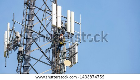 Communication maintenance works. Technician climbing on telecom tower antenna against blue sky background, copy space.
