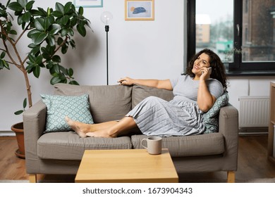Communication, People And Leisure Concept - Happy Young Woman Calling On Smartphone On Sofa At Home