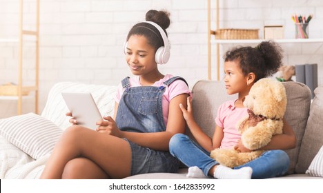 Communication priorities. Teen afro girl chatting with friends online, ignoring her baby sister, panorama - Powered by Shutterstock