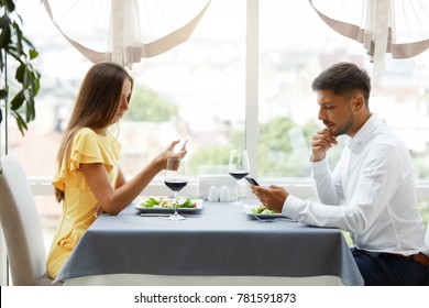 Communication Problem. Man And Woman With Phones On Date. Young Couple Using Cell Phone On Dinner In Luxury Restaurant, Having Relationship Problems. Dating Etiquette. High Resolution.