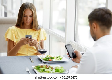 Communication Problem. Man And Woman With Phones On Date. Young Couple Using Cell Phone On Dinner In Luxury Restaurant, Having Relationship Problems. Dating Etiquette. High Resolution.