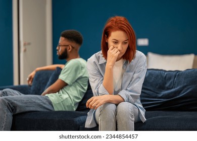 Communication problems in marriage. Upset diverse family couple european wife and african american husband sit separately on sofa at home not talking after fight, having problems in relationships.  - Shutterstock ID 2344854457