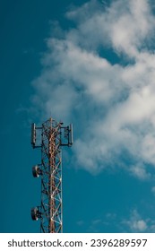 Communication tower on blue sky. top of a cellular repeater tower for 2g 3g and 4g transmission. Cell tower with an antenna in red and white against a blue sky background. - Shutterstock ID 2396289597