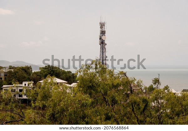 Communications tower behind trees and against a\
cloudy sky