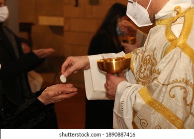 Communion rite during mass in a Catholic church. Priest wears surgical mask due to the Covid-19 pandemic
