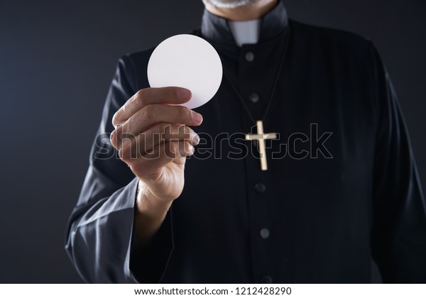 Communion wafer\
hostia priest in hands with\
cross