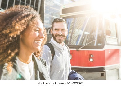 Commuters In The City Walking And Smiling With A Tram On Background. Modern Business Man And Woman Wearing Smart Casual Clothes In The City. Urban Lifestyle