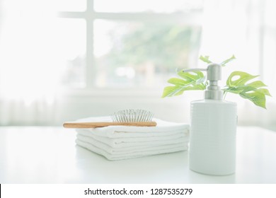 Comp On White Towels And Ceramic Soap, Shampoo Bottles On White Table With Copy Space On Blurred Living Room Background. For Product Display Montage