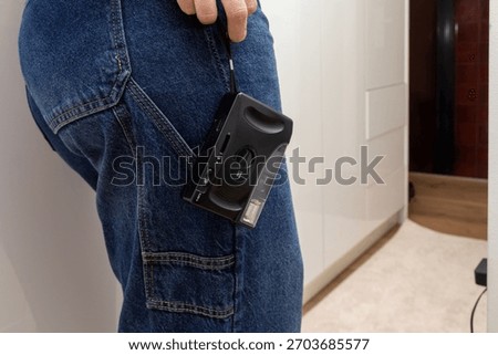 A compact analog camera clipped to the side pocket of blue jeans, showing a practical and stylish way to carry vintage photography gear during everyday movement in a home interior.