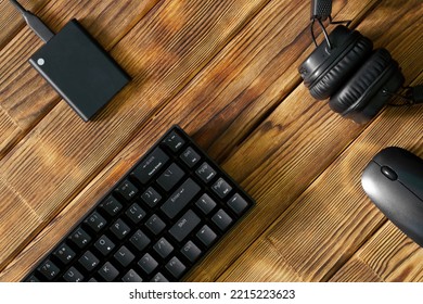 Compact black gaming computer keyboard, headphones, external ssd and computer mouse on a table made of wooden pine boards. Periphery for gadgets and computer. Eco style. Copy space. Daylight - Shutterstock ID 2215223623