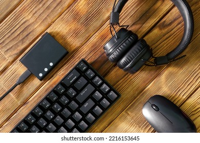 Compact black gaming computer keyboard, headphones, external ssd and computer mouse on a table made of wooden pine boards. Periphery for gadgets and computer. Eco style. Copy space. Daylight - Shutterstock ID 2216153645