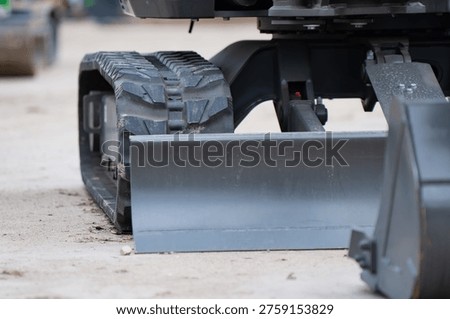 Compact digging machine components showing heavy duty tracks and a metal blade on dirt ground for small scale construction and urban infrastructure development