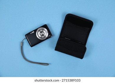 Compact Digital Camera With Wrist Strap And Travel Case On blue Background