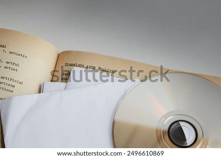 Compact disk and white envelopes and sheets on the background of an opened book with English text, offline learning