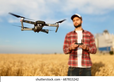 Compact drone hovers in front of farmer with remote controller in his hands. Quad copter flies near pilot. Agronomist taking aerial photos and videos in a wheat field. Innovations in agriculture