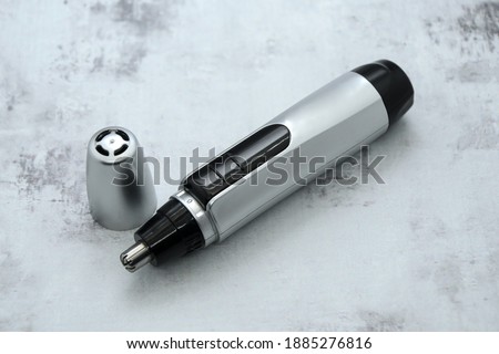 Compact electric nose and ear hair trimmer with cap on gray background. Removal unwanted hair of nose, ear and facial. Trim edge of beard, mustache, eyebrows. Selective focus and blurred background