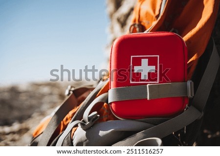 A compact first aid kit attached to a vibrant orange backpack, ideal for outdoor enthusiasts, ensuring safety during hiking and camping trips