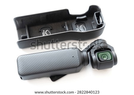 A compact handheld gimbal camera with its protective carrying case is displayed against a white background