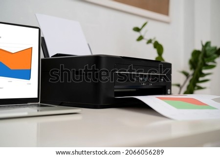 Compact laser home printer. Printers and laptops placed on the desk working on printing documents
