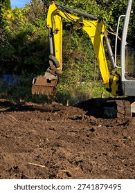 Compact mini excavator performing digging and ground preparation work at a small construction or landscaping site.