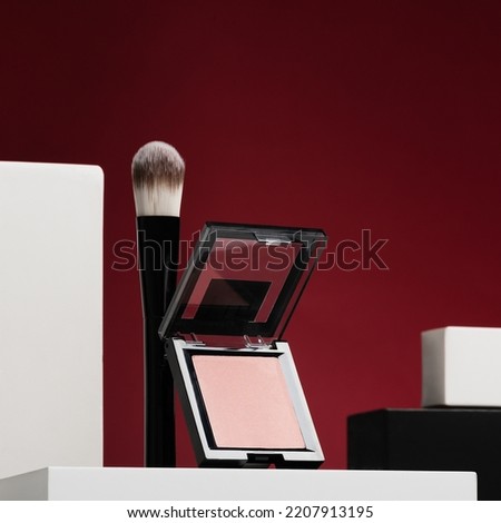 Compact powder case and brush on stand in studio closeup. Blush cosmetic powder with applicator on red background. Supplies for stylish makeup