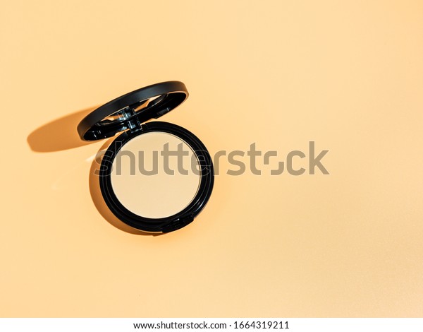 Compact powder\
on yellow or cream background. Female pressed powder in ajar opened\
black plastic case with mirror, copy space right for text or\
design. Hard light. Top view or flat\
lay