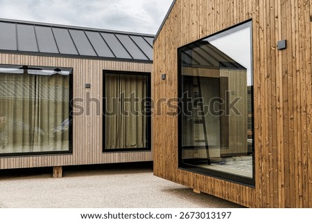 Compact prefab tiny house with timber cladding, large glass window, and minimalist Scandinavian-inspired design, offering eco-friendly and sustainable modern living solutions
